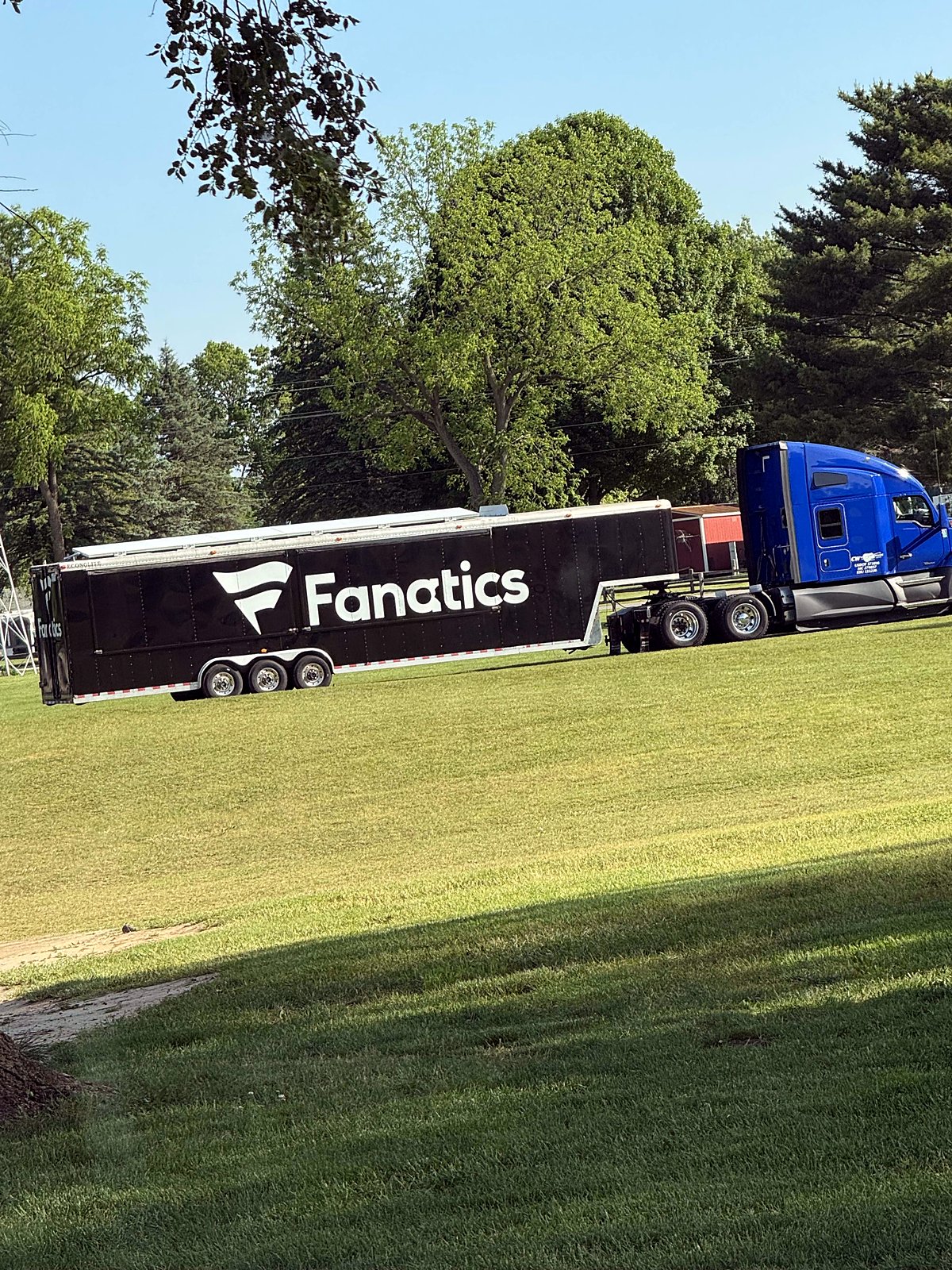 Fanatics trailer and blue tractor on a grass lot